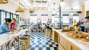 A cafe with checkered flooring, wooden stools, and a variety of baked goods displayed on the counter. - Plum Perfect | Cozy SoCo Stay + Yard & Style (Austin)