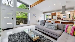 A modern living room with a grey sofa, a glass coffee table, and a black and white rug. - Plum Perfect | Cozy SoCo Stay + Yard & Style (Austin)