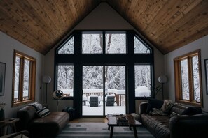 Un intérieur chaleureux avec un plafond haut, de grandes fenêtres et une vue sur une terrasse extérieure enneigée.