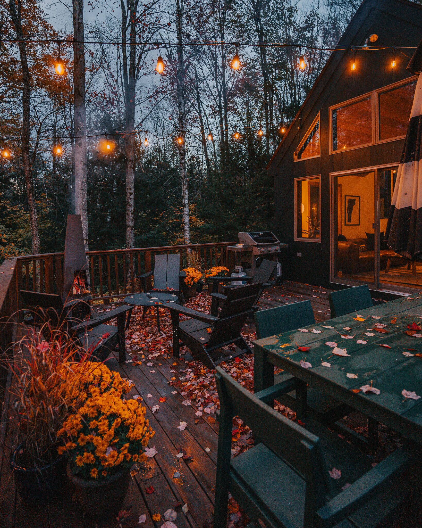Een terras buiten met een barbecue, zitplaatsen en lichtjes.