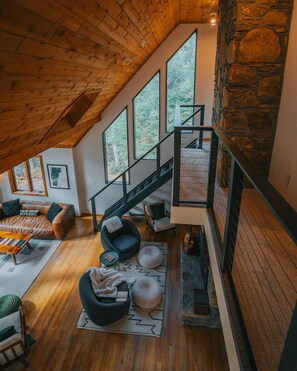 A spacious loft with a high ceiling, large windows, a stone wall, and a modern staircase.