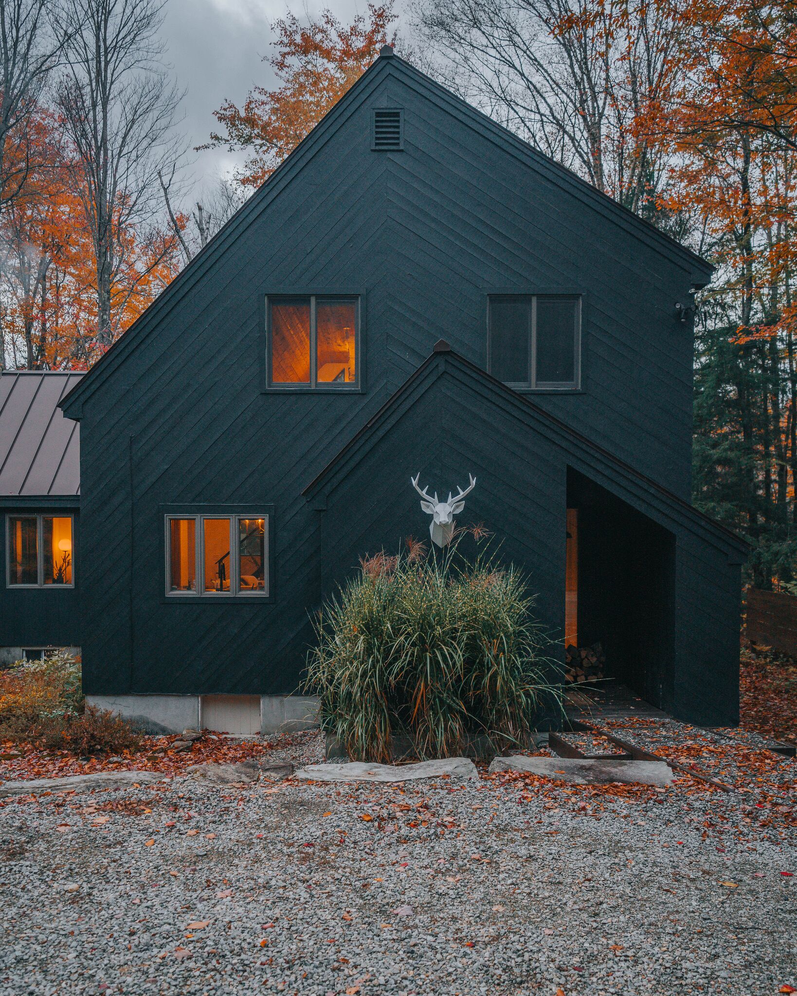 A dark-colored house with a deer head sculpture in front, surrounded by autumn leaves.