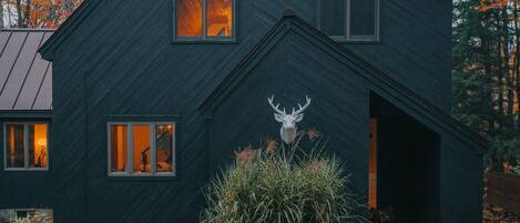 A dark-colored house with a deer head sculpture in front, surrounded by autumn leaves.