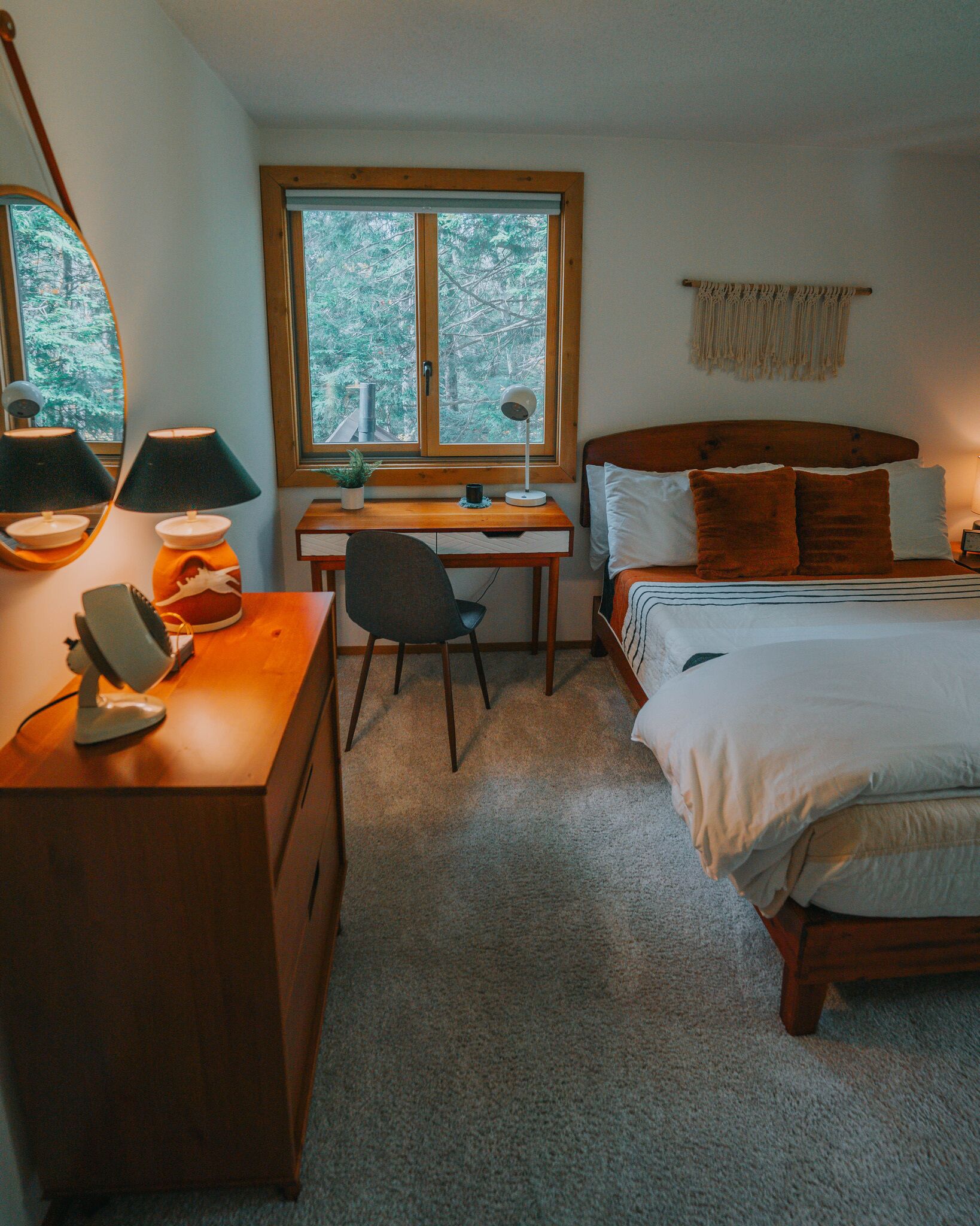 A bedroom with a bed, desk, chair, and a window with a view of trees.