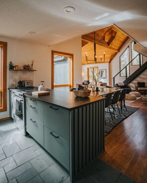 Une cuisine moderne dotée d’un îlot central, de planchers en bois et offrant une vue sur l’espace de vie.