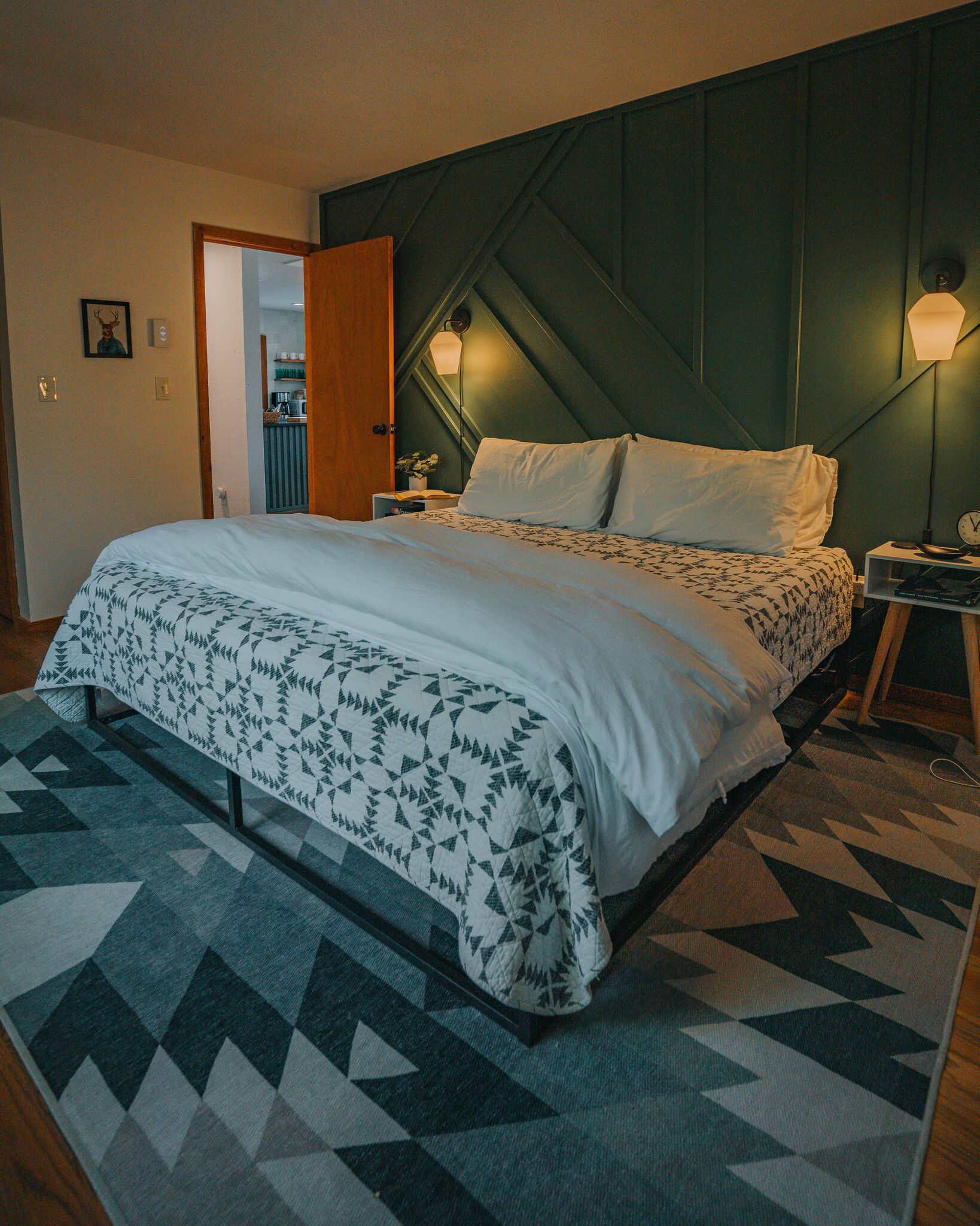 Ein Schlafzimmer mit einem Bett, einem Nachttisch, einer Wandlampe und einem Teppich mit Muster.