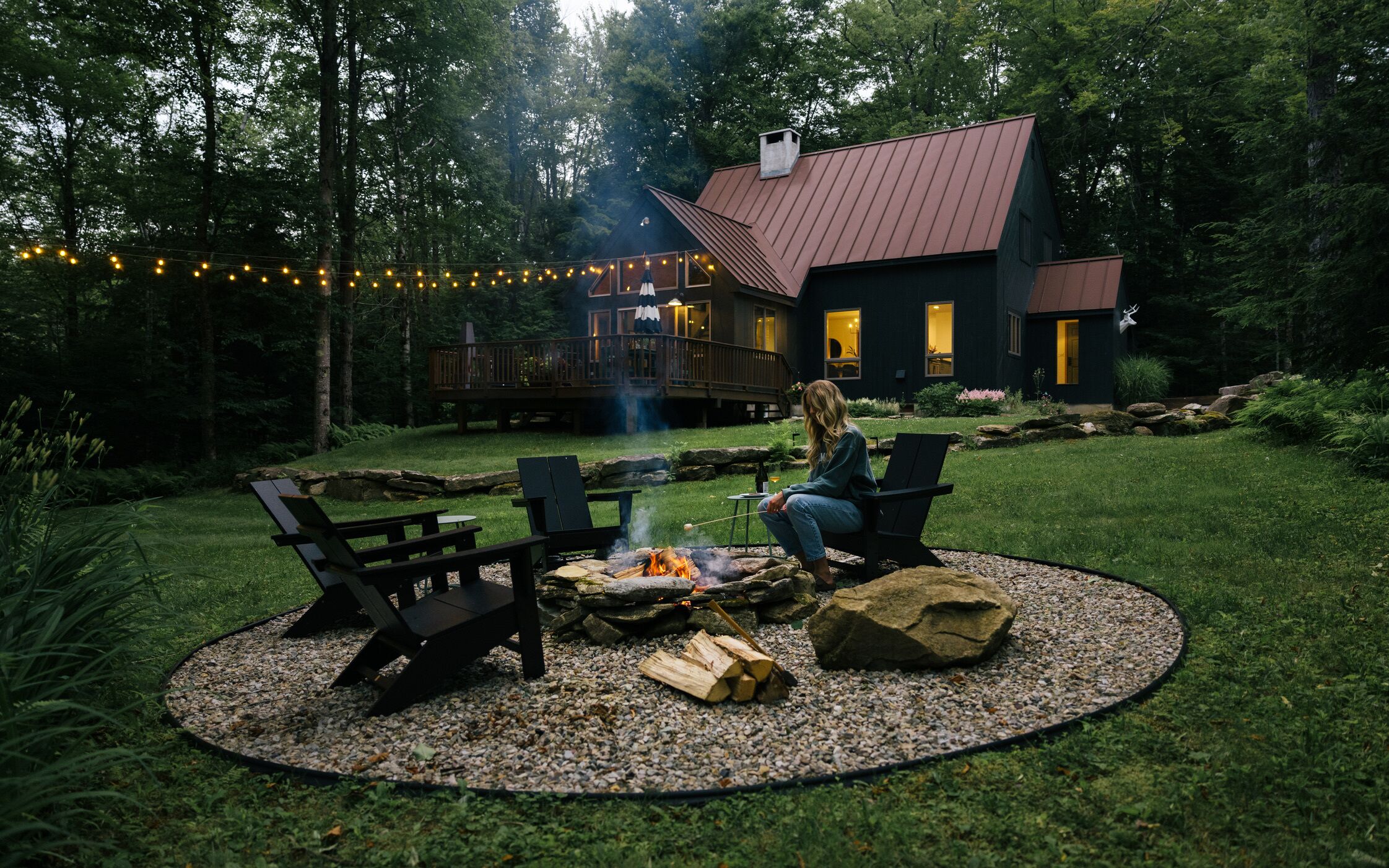 Patio con una chimenea, dos sillas Adirondack y una terraza que da a una casa con techo de metal.