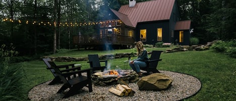 Patio con una chimenea, dos sillas Adirondack y una terraza que da a una casa con techo de metal.