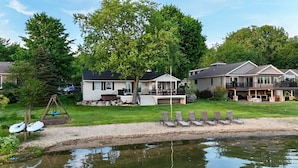 A lakeside property with multiple houses, a swing set, and a pool area with lounge chairs.