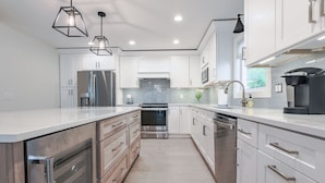 A modern kitchen with white cabinetry, stainless steel appliances, and pendant lighting.