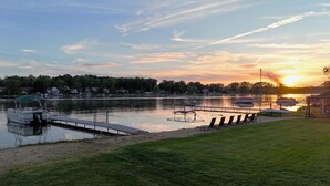 A lakeside view with boats docked, a grassy area, and a sunset in the background.