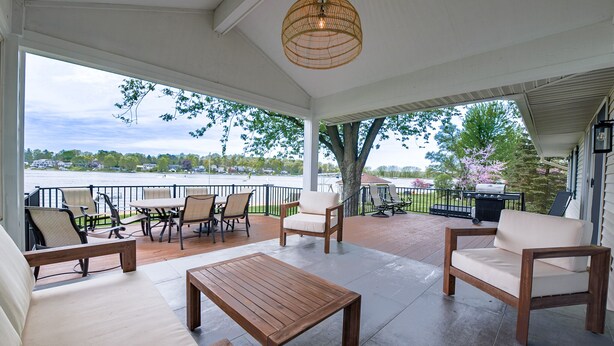 A covered patio with outdoor furniture, a wooden table, and a hanging light fixture.