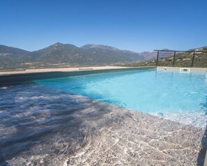 Une piscine à l’eau d’un bleu cristallin, entourée de montagnes et avec une plage en arrière-plan.