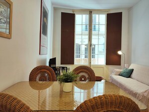 A room with a dining table, chairs, a sofa, a lamp, and a window with shutters.