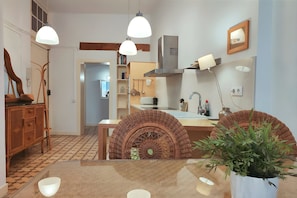 A modern kitchen with pendant lighting, a central island, wicker furniture, and a potted plant.