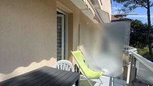 Een balkon met een tafel, stoelen, een deur en uitzicht op bomen.