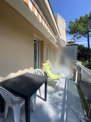 A balcony with a table and chairs, a door, and a view of trees. - PORNICHET CENTRE GARE (PORNICHET)
