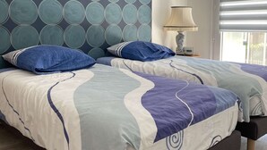 Een slaapkamer met twee bedden, een behang met patroon, een lamp en een raam met zonwering.