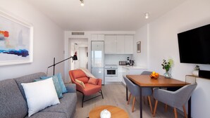 Een moderne woonkamer met een grijze bank, een rode fauteuil, een houten salontafel en een eethoek met grijze stoelen.