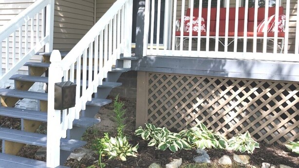 A front porch with a wooden staircase, a red cushioned bench, and a lattice fence. - Dog Friendly|Fenced|Full Kitchen|Firepit (Alpena)