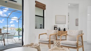 Un salon moderne doté d’une porte vitrée donnant sur un balcon, d’une table basse ronde, de deux fauteuils confortables et d’une petite table d’appoint sur laquelle se trouve une machine à café.