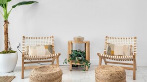 Une pièce au décor minimaliste, avec deux chaises en bois, une petite table surmontée d’un panier en osier et une plante en pot.