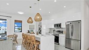 Une cuisine moderne dotée d’un îlot central, d’appareils électroménagers en acier inoxydable et d’un coin repas avec des chaises en bois.