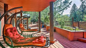 A wooden deck with two lounge chairs, a wooden fence, and a view of trees.