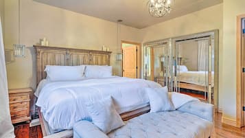 Un dormitorio con una cama grande, un banco, una araña y un espejo.