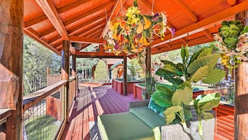 Una terraza de madera con un arreglo floral colgante, un sofá de mimbre y vistas de la vegetación circundante.