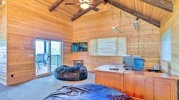 A log cabin interior with a ceiling fan, a large window with blinds, a television, and a desk with a chair.