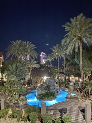 Une vue nocturne d’un complexe hôtelier avec une piscine entourée de palmiers et un bâtiment dont l’enseigne est illuminée.