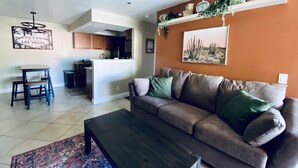 Sala de estar com sofá, mesa de centro e área de cozinha ao fundo.