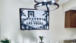 Uma área de jantar com uma mesa de madeira posta para quatro pessoas, uma planta em vaso e uma placa emoldurada acima.