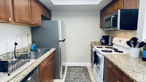 Cozinha compacta com armários de madeira, geladeira de aço inoxidável, micro-ondas, fogão e lava-louças.