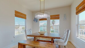 Un comedor con mesa y sillas de madera, una lámpara colgante y ventanas con persianas.