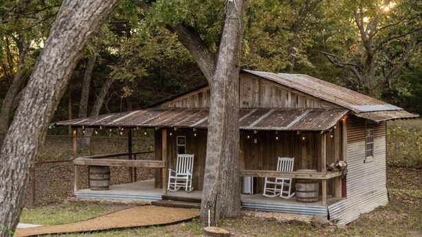 A rustic cabin with a porch, wooden chairs, and a barrel. - Secluded Country Retreat- Hot Tub & Fire Pit-3BR minutes to Z-Plex and Downtown  (McKinney)