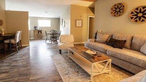 A spacious living room with a wooden floor, a sofa set, a coffee table, and a dining area with chairs and a table. - Secluded Country Retreat- Hot Tub & Fire Pit-3BR minutes to Z-Plex and Downtown  (McKinney)