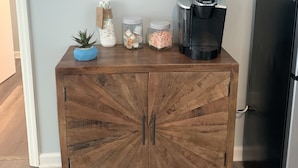 Un mueble de madera con una cafetera, frascos y una pequeña planta.