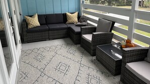 Un espacio al aire libre cubierto con un sofá modular y sillones de mimbre, un cuadro decorativo de peces en la pared, y vistas al exterior.
