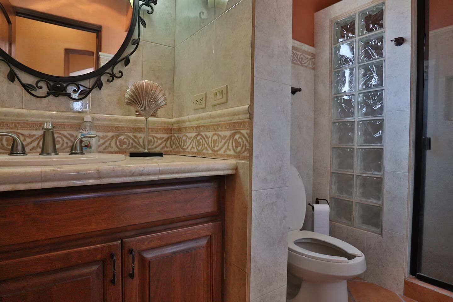 A bathroom with a marble vanity, a sink with three faucets, a mirror with an ornate frame, a toilet, and a window with frosted glass.