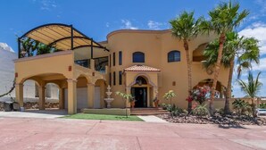 Un edificio de varios pisos con entrada techada, palmeras y una fuente.