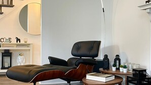 Una sala de estar moderna con una lámpara de techo curva, un sillón de cuero negro, una mesa de centro de madera y una escalera al fondo.