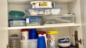 Ein weißes Schranksystem mit Regalen, das Aufbewahrungsbehälter, Plastikbecher und eine Mr. Coffee Kaffeemaschine enthält.