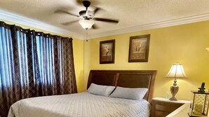 Ein Hotelzimmer mit einem Bett, einem Sessel, einem Nachttisch mit Lampe und einem Deckenventilator.