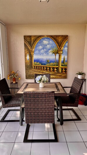 Een eetgedeelte met een tafel, stoelen en een groot schilderij van een boog met uitzicht op een landschap.