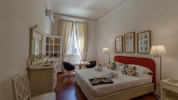 Une chambre d’hôtel comprenant un lit, une table de chevet, une chaise, un bureau et une fenêtre avec des rideaux.