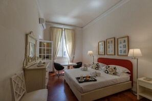 Une chambre d’hôtel comprenant un lit, une table de chevet, une chaise, un bureau et une fenêtre avec des rideaux.