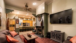 A living room with a fireplace, a sofa, and a coffee table. There is a kitchen in the background with a bar and stools.
