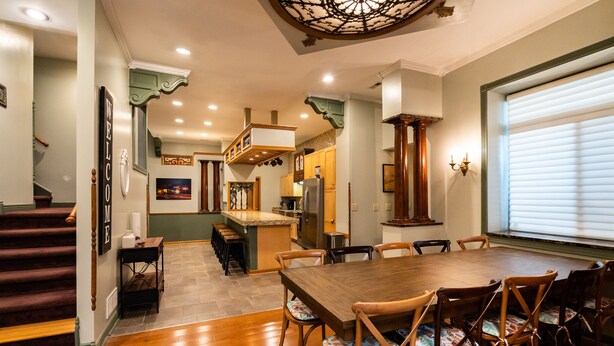 A spacious dining area with a wooden table and chairs, a kitchen in the background, and a staircase leading to another level.